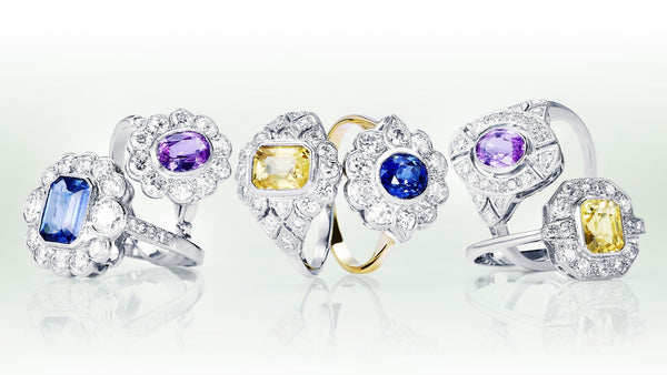 Six coloured gemstone and diamond cluster rings in a row, showing emerald-cut and oval stones